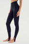 A person wearing SPLITS59 River High Waist Airweight Stirrup leggings in black stands barefoot against a plain light-colored background.