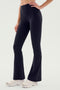 A person is wearing SPLITS59 Raquel High Waist Airweight Flare pants in black and white sneakers, photographed from the waist down. The person has one hand resting on their hip.