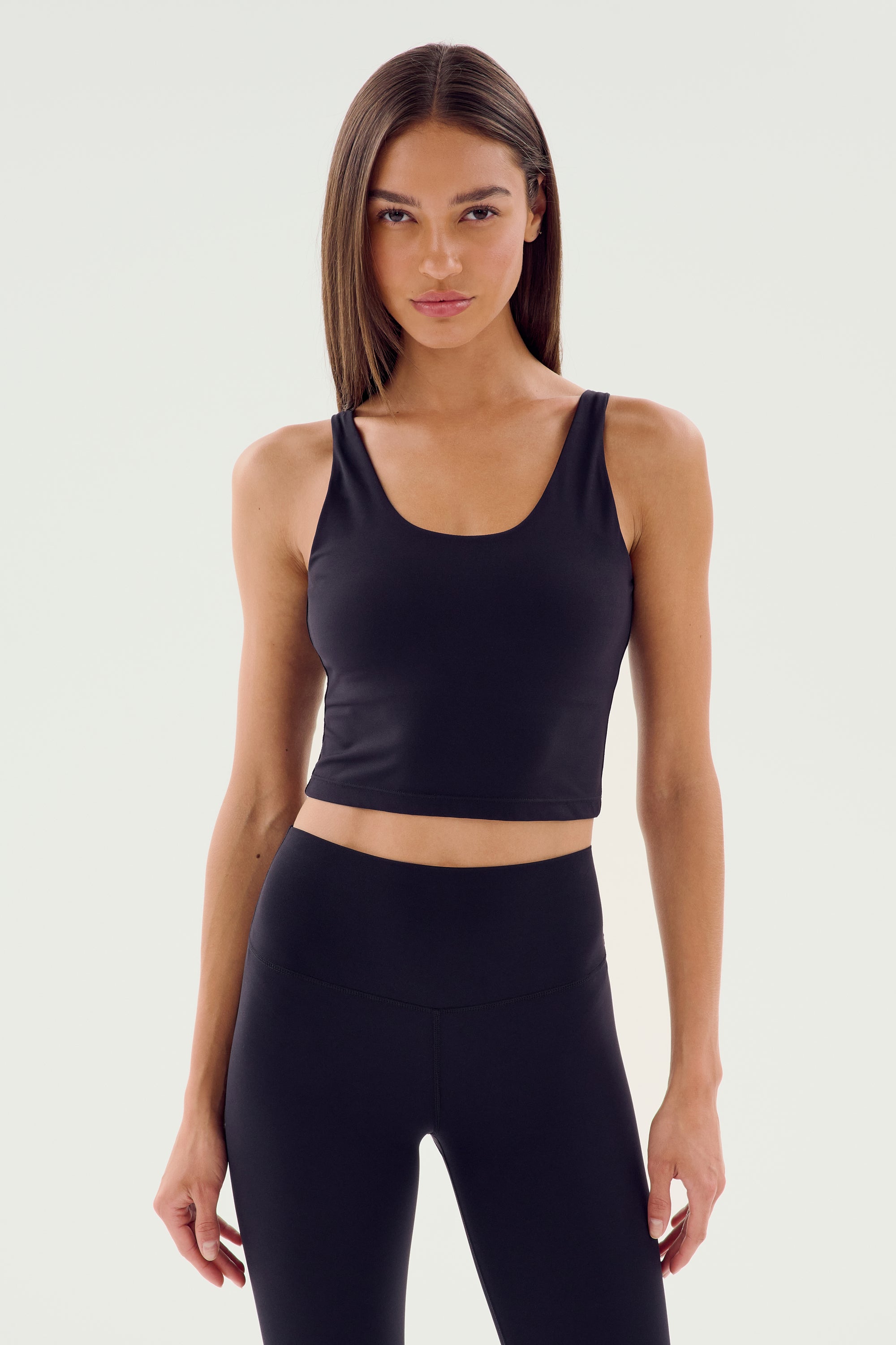 A person with long hair is wearing the Sprint Rigor Bralette in black from SPLITS59 alongside matching leggings against a plain background, showcasing multi-sport performance.