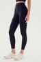 A person, dressed in Sprint High Waist Rigor 7/8 leggings by SPLITS59 and white athletic shoes, stands against a plain background ready for gym workouts.