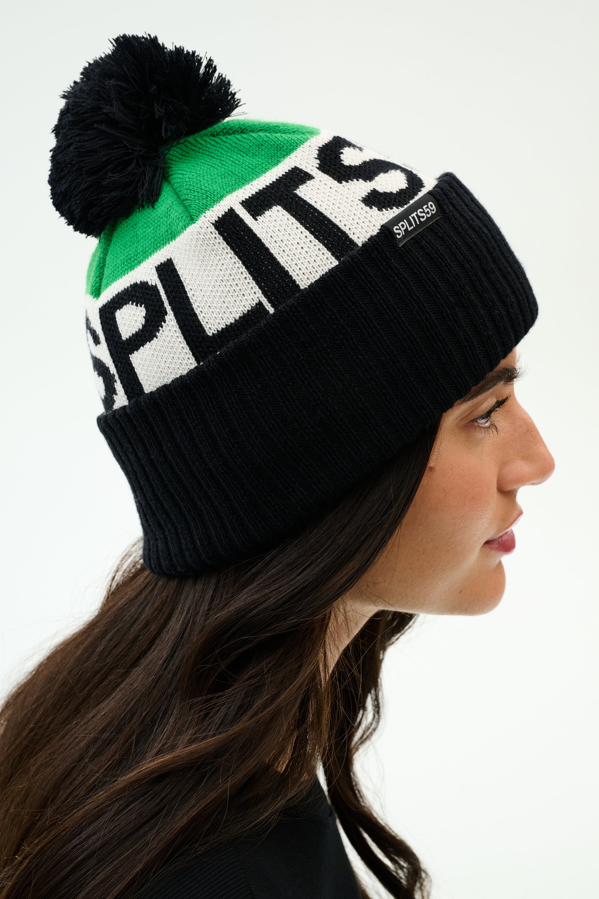 A person in profile wearing a green, white, and black beanie with a pom-pom and the word "SPLITS59" knitted on the hat.