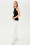 Full front side view of woman with blonde straight hair wearing white high waist below ankle length legging with wide flared bottoms with split hem flare opening and black racerback tank top. Paired with white and gray shoes.