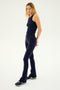 A woman stands against a plain background, wearing a black sleeveless top, the SPLITS59 Raquel High Waist Flared Legging in Indigo made from 4-way stretch supplex fabric, and black and white athletic shoes. She has long blonde hair and is looking towards the camera, embodying the Raquel yoga style.