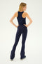 A woman stands with her back to the camera, hands on hips, wearing the SPLITS59 Kiki Rib Crop Tank in Indigo and navy blue high-waisted flare pants.