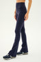 A person wearing SPLITS59's Raquel High Waist Flared Legging in indigo and athletic shoes stands against a plain background.