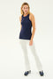 A person stands wearing the Kiki Rib Tank Full Length - Indigo by SPLITS59, paired with white pants and dark sneakers against a plain white background, ready for some yoga or gym workouts.