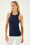 A woman with long blonde hair wearing the SPLITS59 Kiki Rib Tank Full Length in Indigo and white pants stands against a plain background, embodying the elegance of yoga.