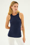 A woman with long blonde hair wears the SPLITS59 Kiki Rib Tank Full Length in Indigo, featuring a high racer neckline, paired with white leggings. She is looking to her right with a neutral expression against a plain background, evoking the essence of dedicated gym workouts.