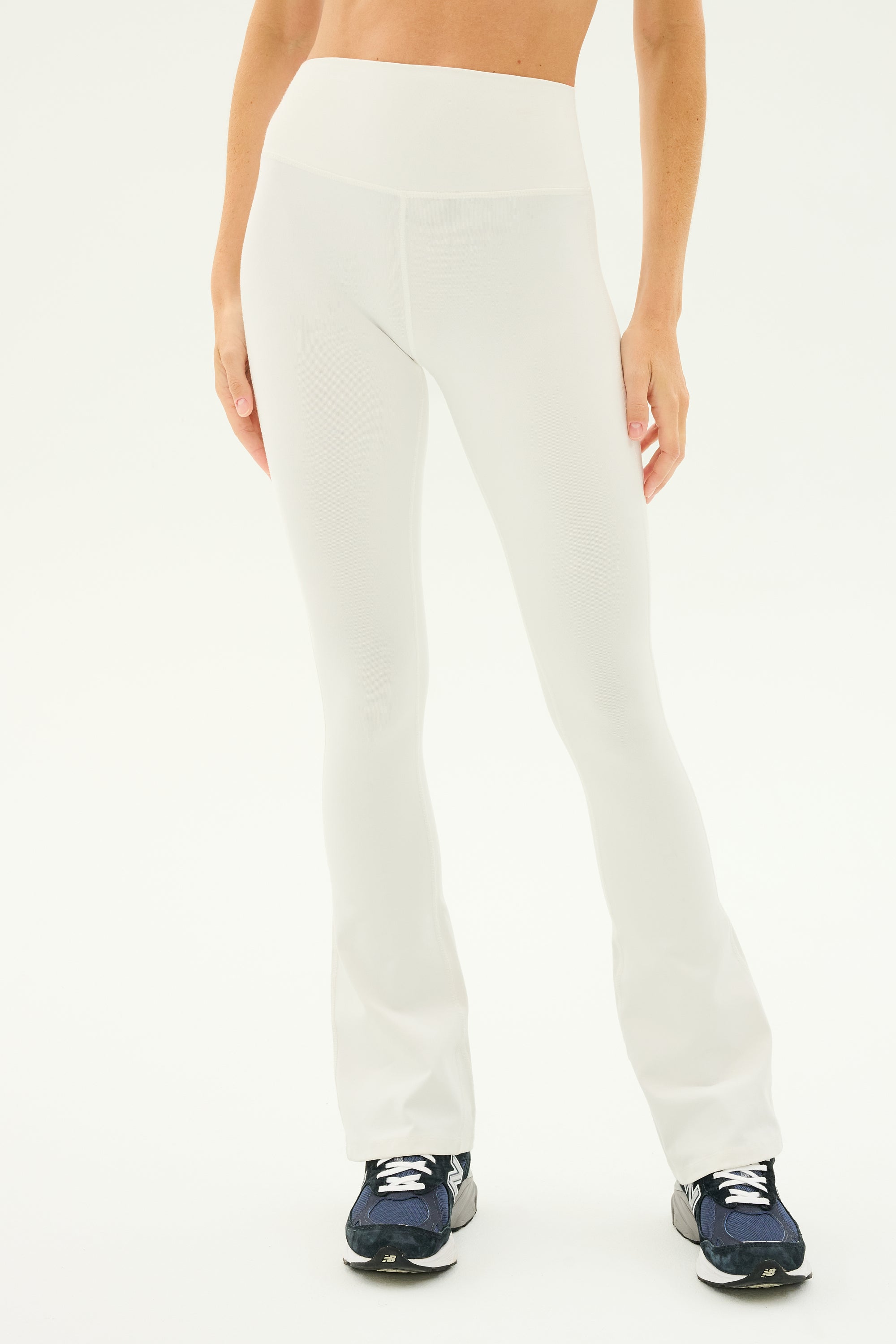 A person is shown wearing the Raquel High Waist Flared Legging in white by SPLITS59, made from 4-way stretch supplex fabric, paired with black athletic shoes. The background is plain white.
