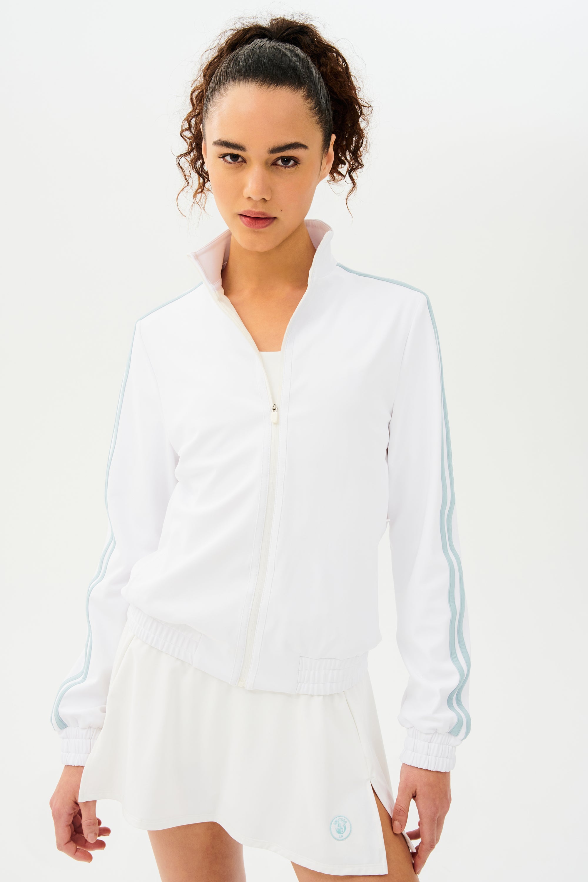 A woman wearing a SPLITS59 Fox Techflex Jacket in White/Teal and skirt, giving off a retro vibe.
