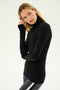 A person with long hair wearing a black Jackson Rib Full Length Turtleneck by SPLITS59 and gray leggings stands against a plain background.