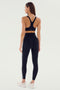 A woman faces away, wearing the SPLITS59 Ella High Waist Airweight 7/8 leggings in Black/White and a matching sports bra, paired with white sneakers against a plain light background.