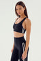 A woman in an Ella Airweight Bra by SPLITS59 and high-waisted leggings with white side stripes stands against a plain background.