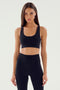 Person wearing a black Ella Airweight Bra by SPLITS59 and black high-waisted leggings, standing with arms relaxed by their sides.