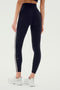 A person wearing SPLITS59 Ella High Waist Airweight 7/8 leggings in Black/White with white side stripes and white sneakers stands on a light surface, viewed from the back—ideal for hot yoga.