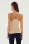 A woman with long hair wearing the SPLITS59 Loren Seamless Waist Length Tank in Nude and black leggings, facing away from the camera against a light background.