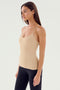 A woman with long hair is standing slightly to the left against a plain white background, ready for her gym workouts. She is wearing the SPLITS59 Loren Seamless Waist Length Tank in Nude and black leggings.