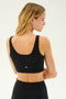A person with long blonde hair is standing with their back to the camera, wearing a black Sprint Rigor Bra from SPLITS59 and black leggings, perfect for multi-sport performance.