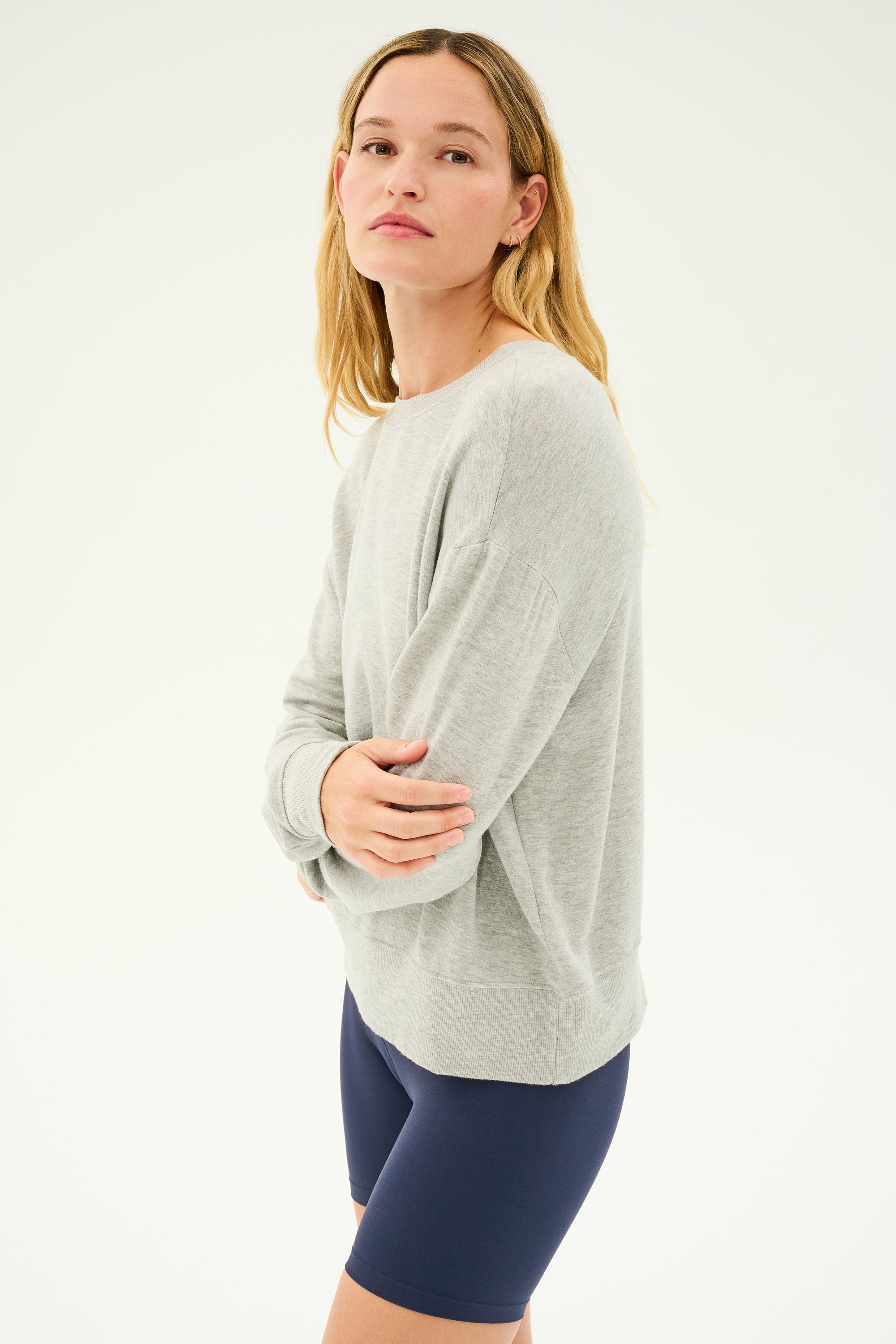 Person standing against a plain background wearing an SPLITS59 Sonja Fleece Sweatshirt in Heather Grey and navy blue shorts MADE IN LOS ANGELES.