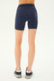 Person wearing indigo Airweight High Waist Shorts by SPLITS59 and sneakers, viewed from the back against a plain white background, ready for a dynamic Pilates session.