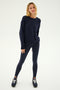 A woman stands against a plain background wearing SPLITS59's River High Waist Airweight Stirrup leggings in navy, paired with a matching long-sleeve sweatshirt and black sneakers.