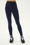 Person wears the SPLITS59 River High Waist Airweight Stirrup legging in Indigo with black athletic shoes, standing against a plain light background—perfect for hot yoga or everyday style.