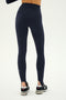 A person wearing SPLITS59 River High Waist Airweight Stirrup leggings in Indigo and black sneakers, shown from the back against a plain light background.