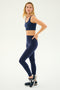A woman wearing the SPLITS59 Sprint High Waist Rigor 7/8 in Indigo and black sneakers stands against a plain background, ready for her workout fitness routine.