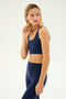 A woman wearing an indigo Sprint Rigor Bra by SPLITS59 and matching high-waisted leggings looks to her left, holding her left hand near her ear.