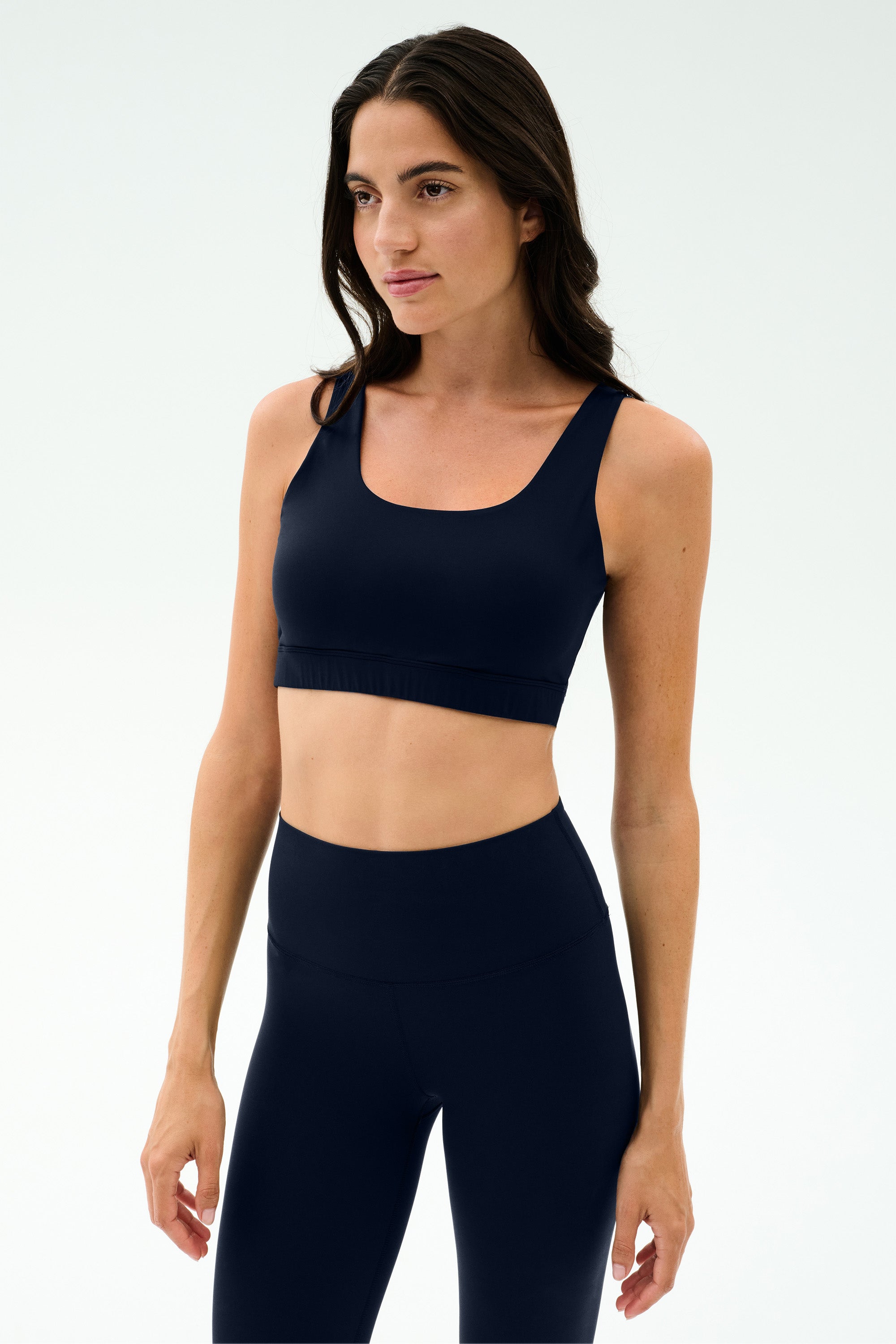 A woman wears the SPLITS59 Sprint Rigor Bralette in Indigo with high-waisted leggings, standing against a plain light background.