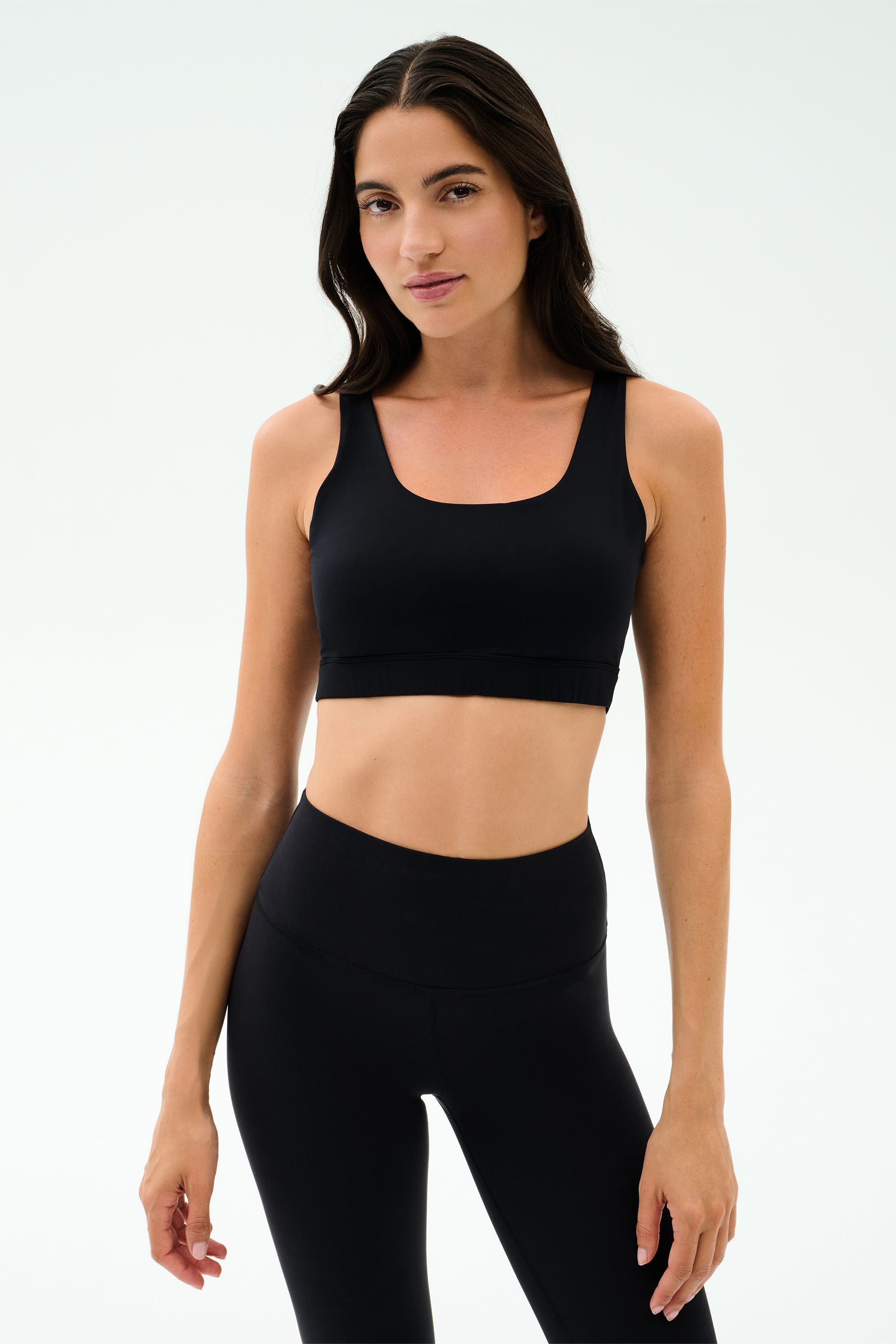 A woman models the SPLITS59 Sprint Rigor Bra in black, standing against a simple light background—ideal for gym workouts or versatile multi-sport performance.