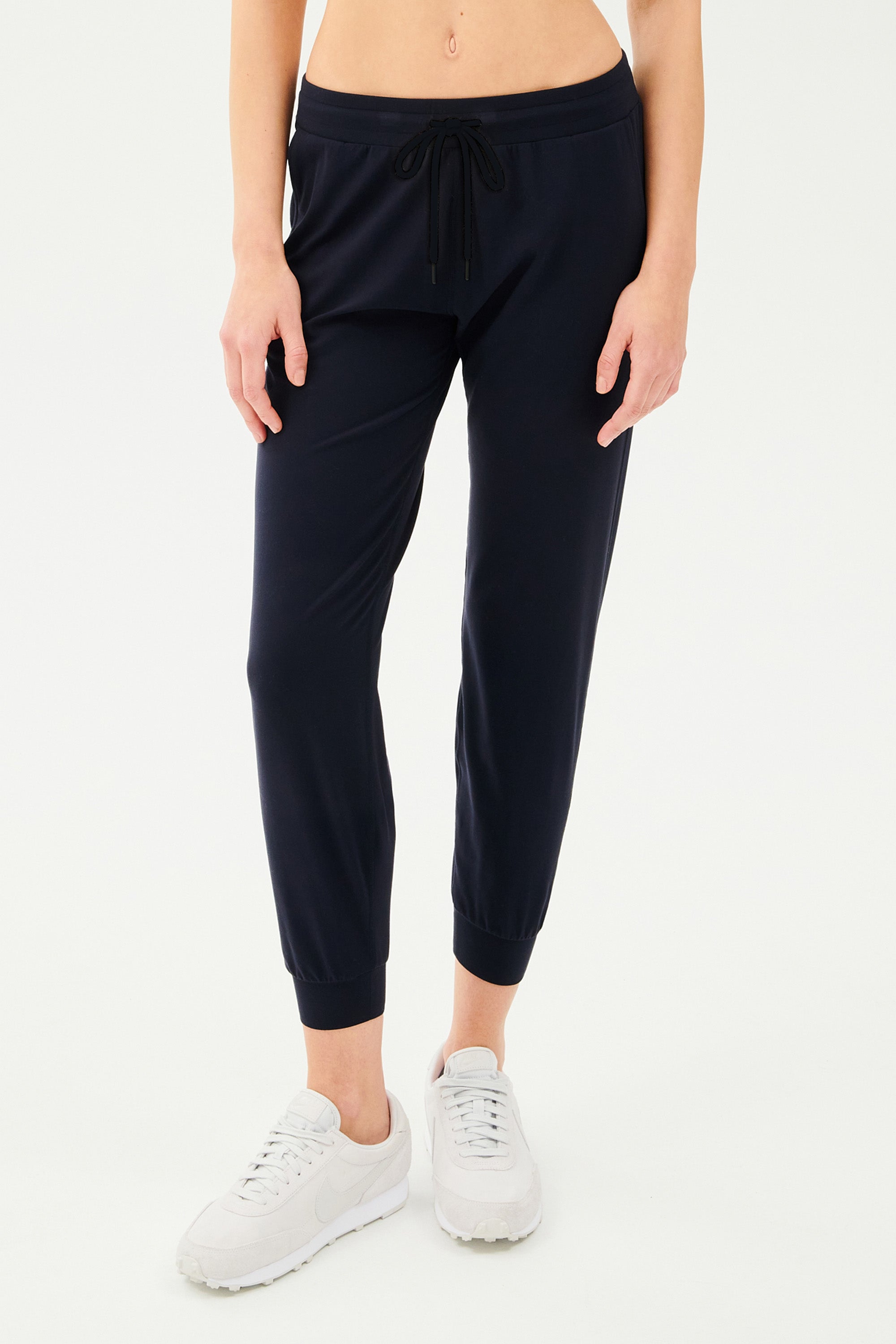 Front view of girl wearing dark blue sweatpants with black tie around waistband with white shoes