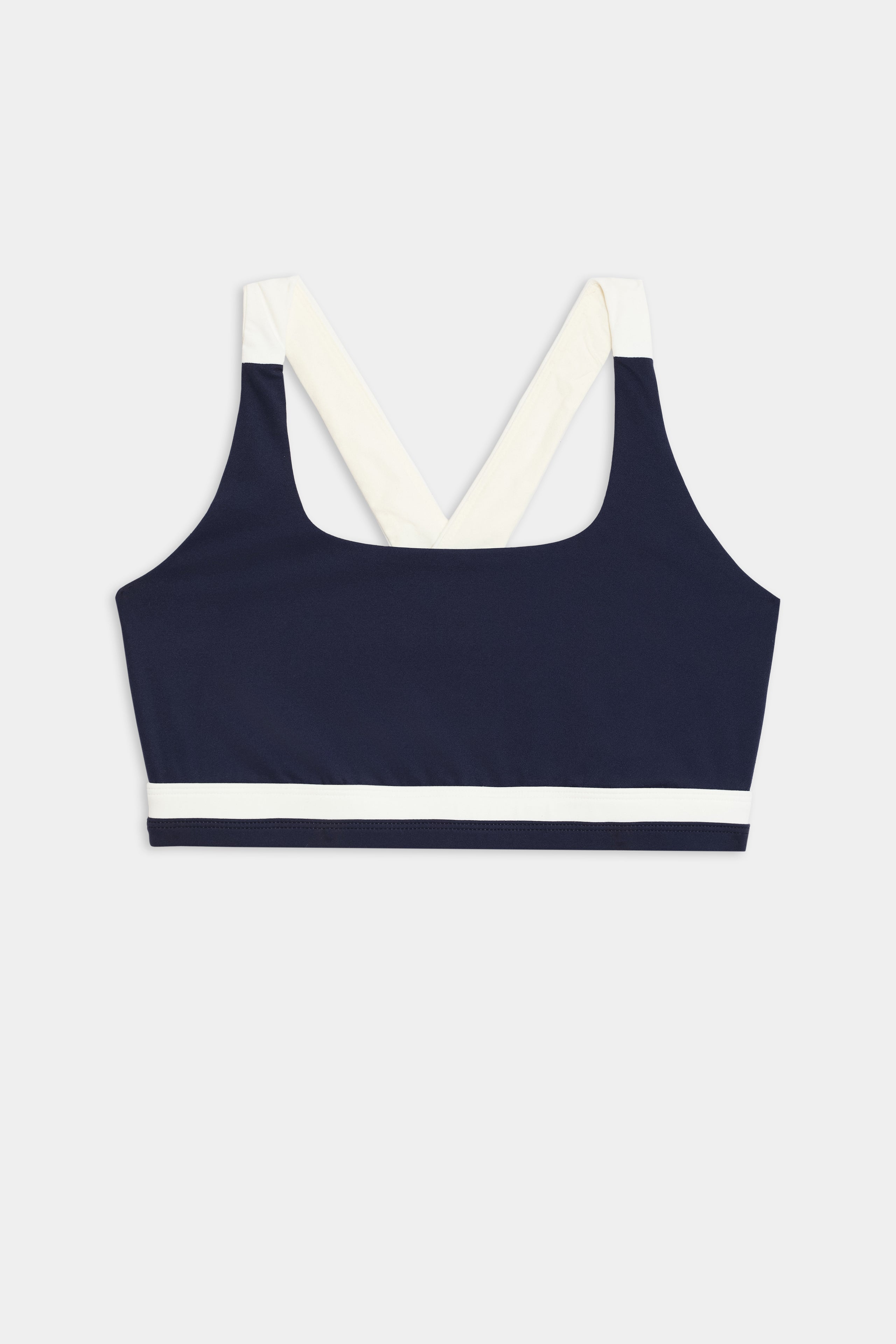 The Miles Rigor Bra by SPLITS59, featuring a navy design with wide white straps and a white band under the bust, is displayed on a light gray background.