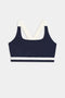 The Miles Rigor Bra by SPLITS59, featuring a navy design with wide white straps and a white band under the bust, is displayed on a light gray background.