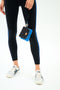Person wearing black leggings with blue stripes and silver sneakers, holding the SPLITS59 MZW x Splits59 Metro Key Pouch Wristlet—a small black and blue quilted handbag—by their side against a plain background.