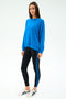 A person wears the SPLITS59 Andie Oversize Fleece Sweatshirt in Classic Blue and black leggings with blue stripes, made from a soft modal spandex blend, paired with white sneakers against a plain white background.