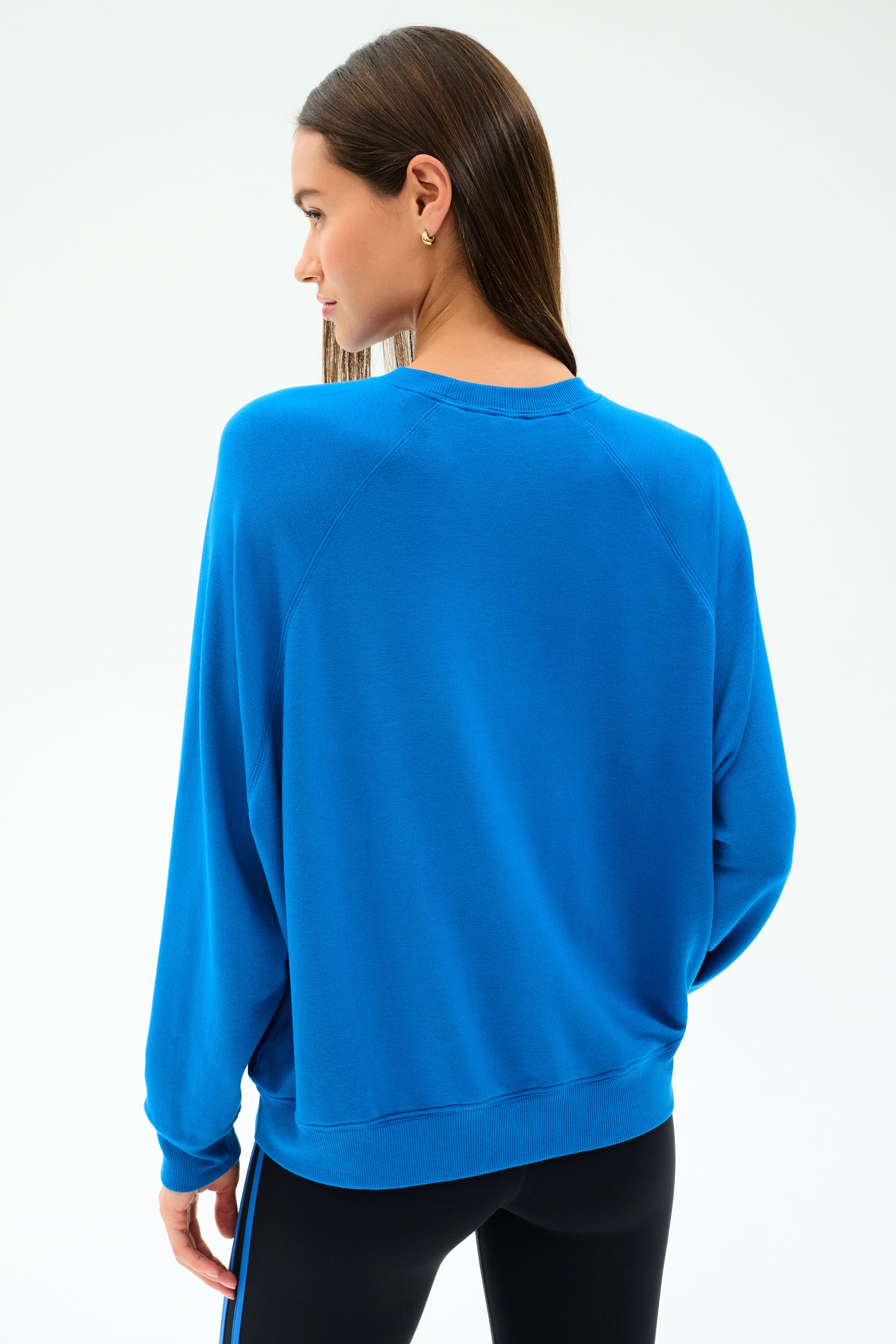 A woman with straight brown hair, seen from the back against a white background, wears the SPLITS59 Andie Oversize Fleece Sweatshirt in Classic Blue with black leggings.