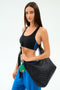 A woman in a black sports bra and blue pants carries the SPLITS59 MZW x Splits59 Carry All, a large black quilted bag with a green and red keychain.