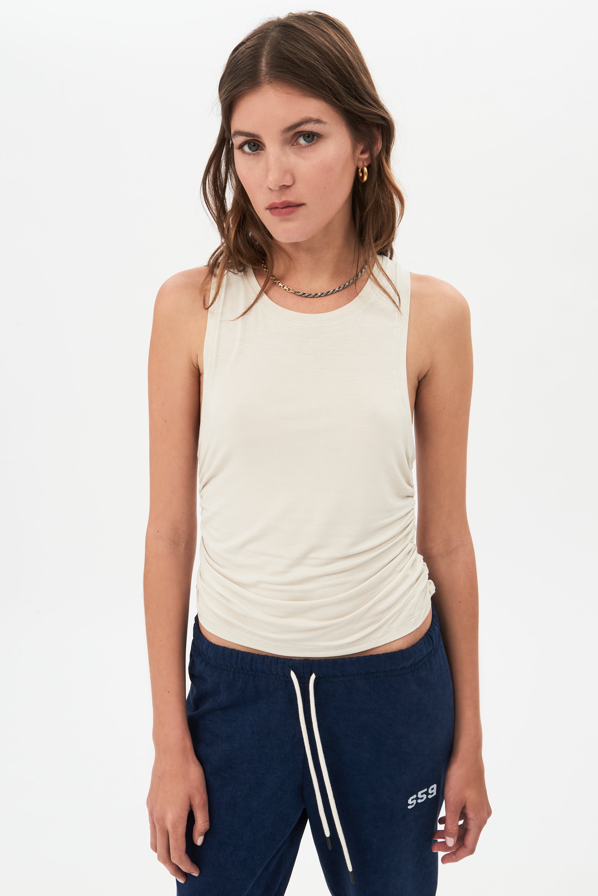 Young woman posing in a SPLITS59 Frida Jersey Tank in Vintage White designed for gym workouts and blue sweatpants.