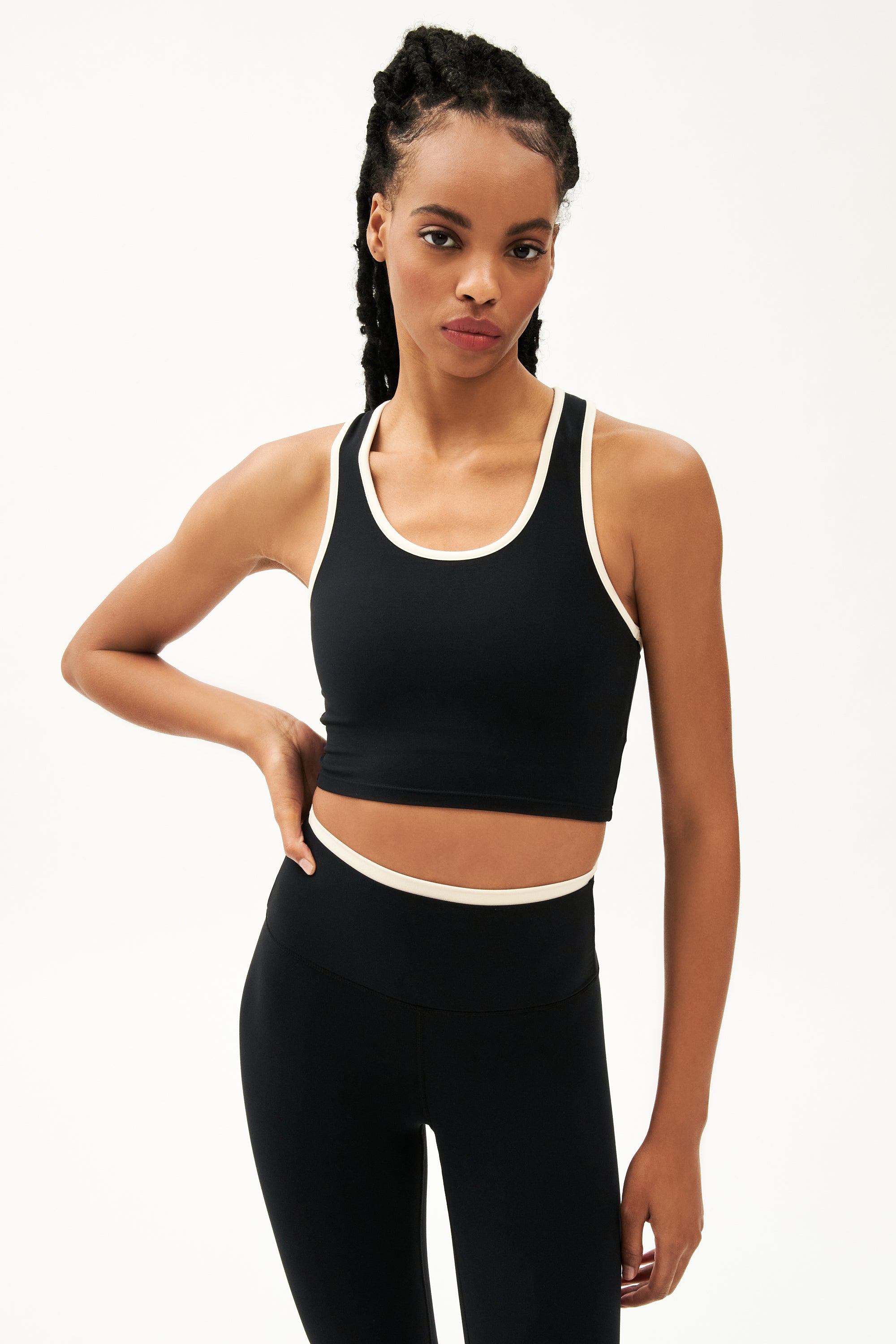 Front view of girl wearing cropped black tank top with white trim and black leggings with a thin white waistband