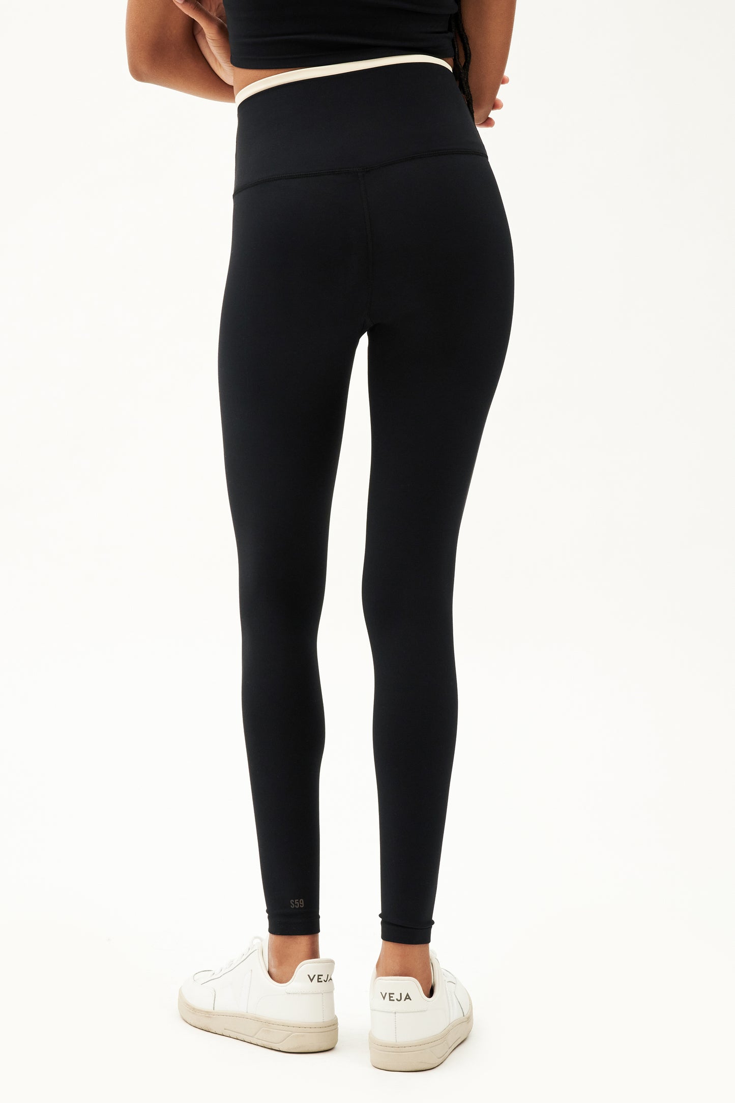 Back view of girl wearing black leggings with thin white band around waist and black tank top with white shoes