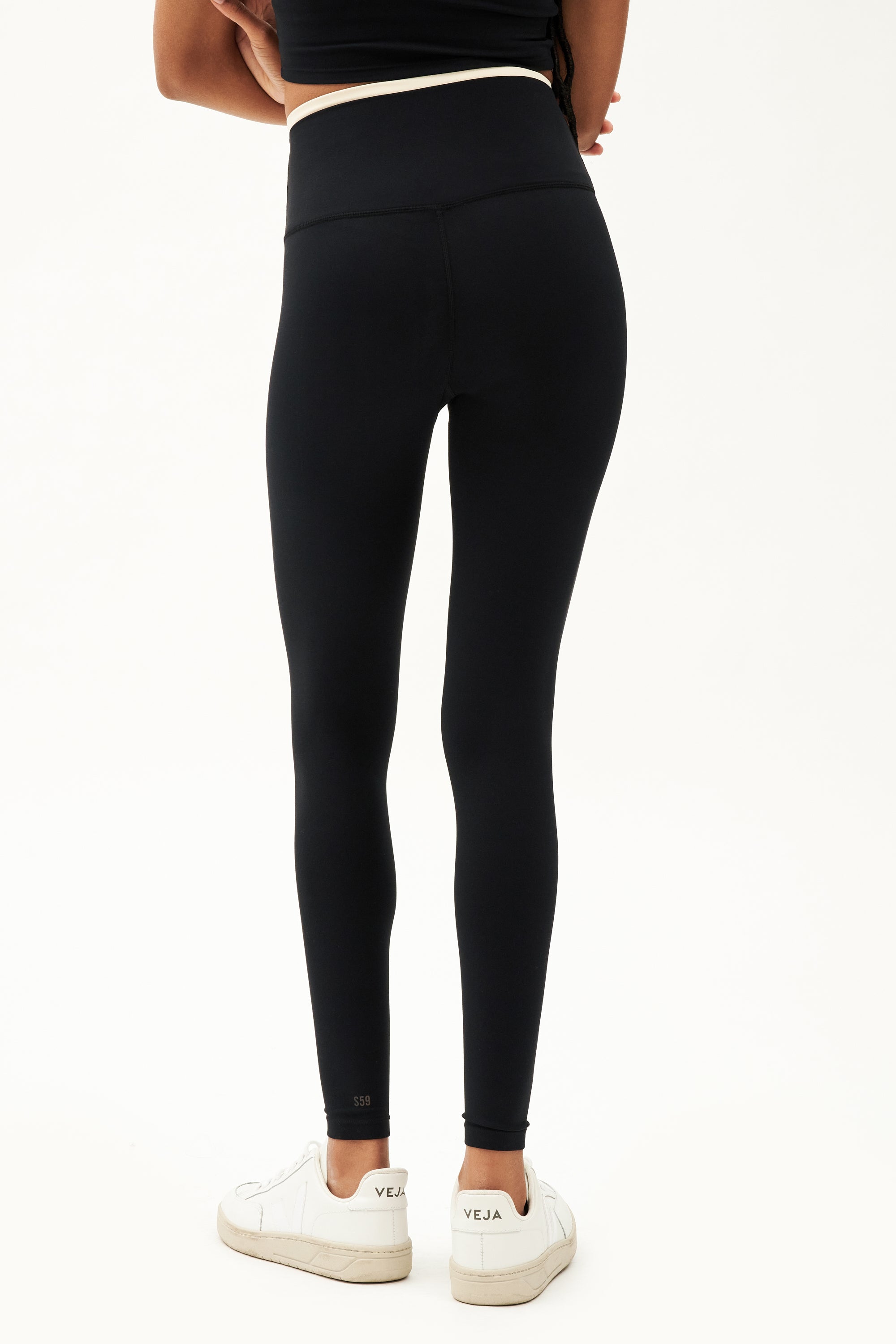 Back view of girl wearing black leggings with thin white band around waist and black tank top with white shoes
