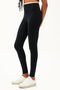 Side view of girl wearing black leggings with thin white band around waist with white shoes