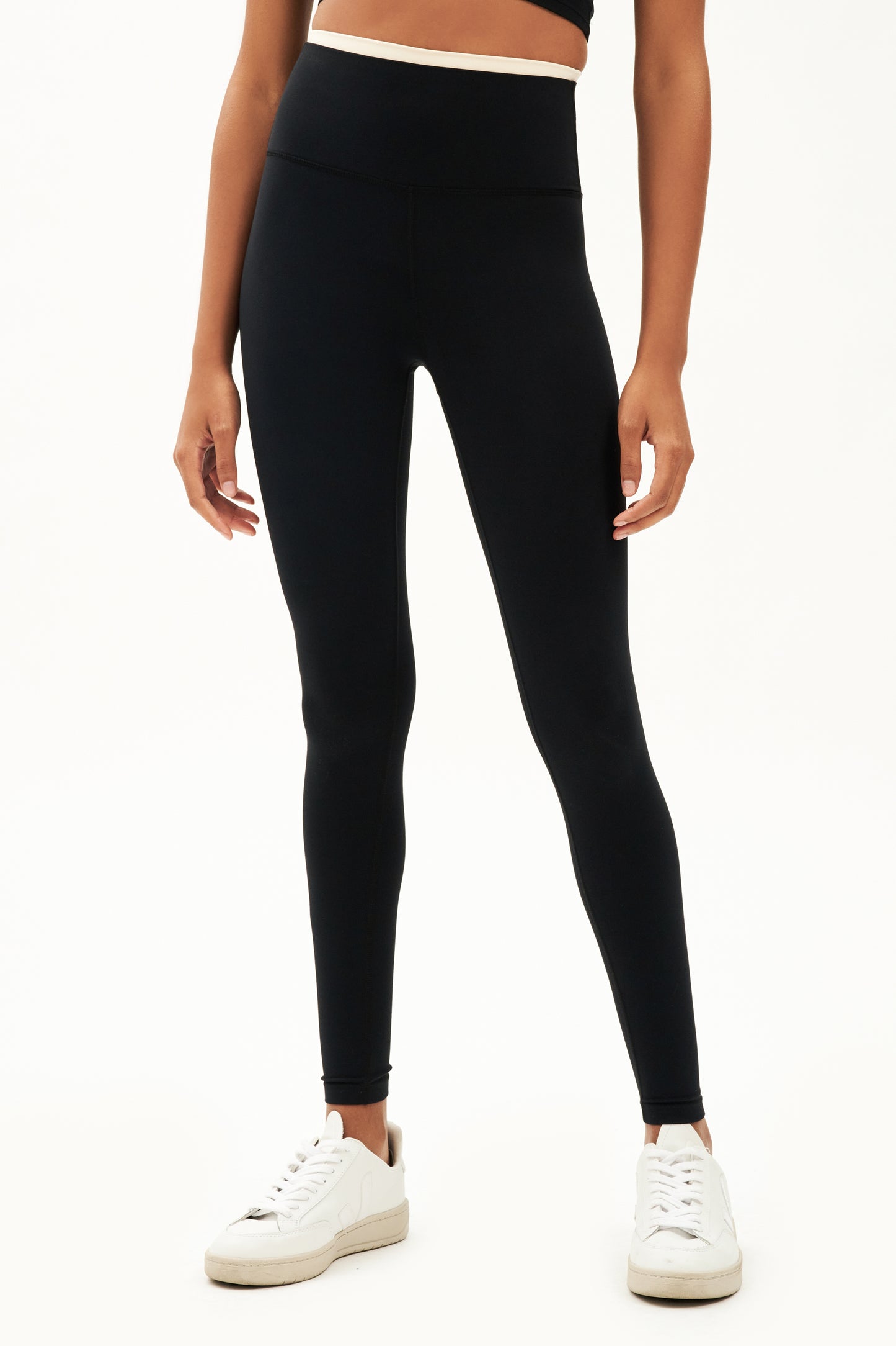 Front view of girl wearing black leggings with thin white band around waist with white shoes