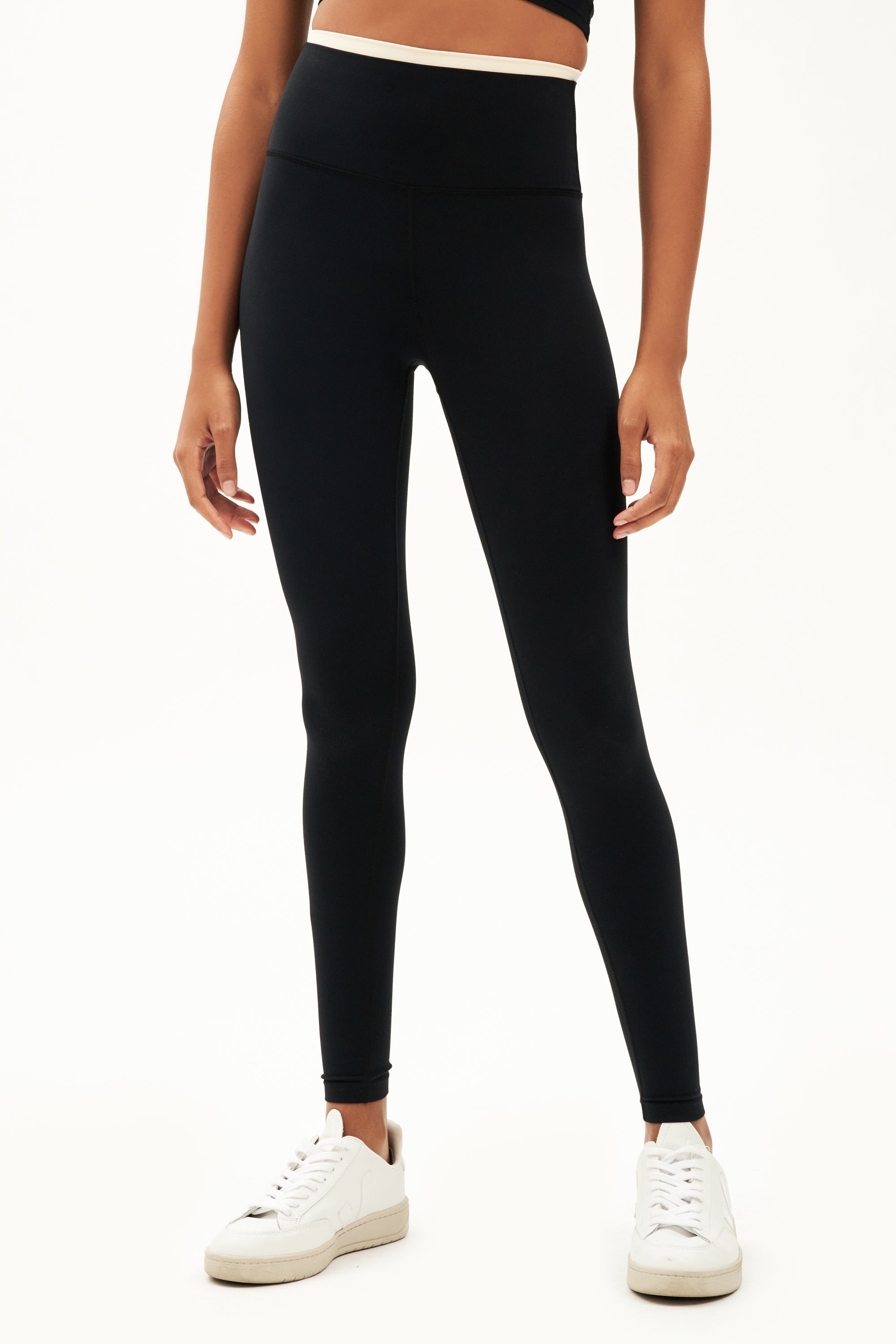 Front view of girl wearing black leggings with thin white band around waist with white shoes