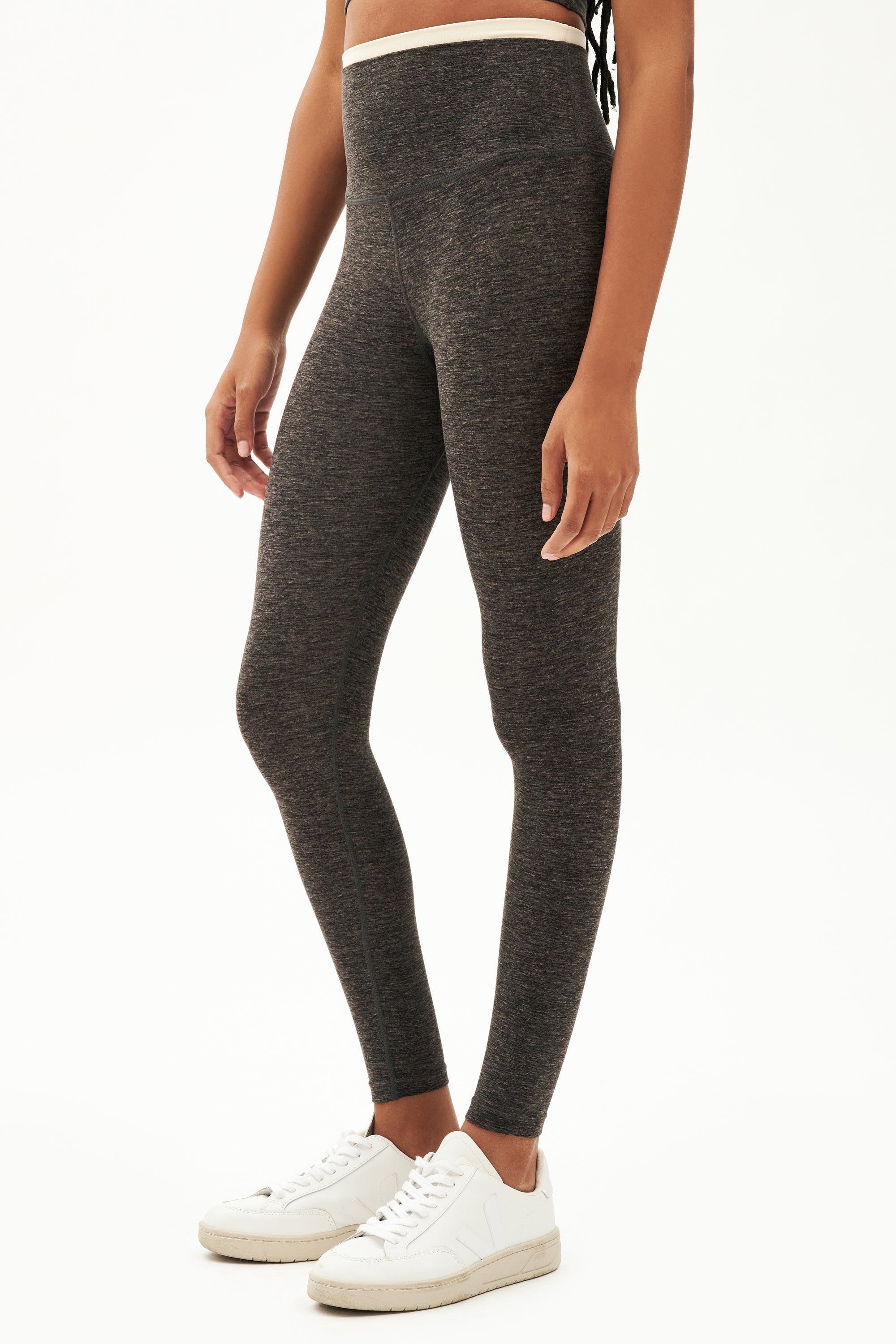 Side view of girl wearing dark grey leggings with thin white band around waist with white shoes