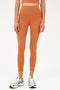 Front view of model wearing a dark orange bra tank with dark orange high waist leggings and white shoes with black stripes
