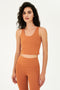 Front view of woman with curly dark brown hair wearing a dark orange bra tank  with dark orange leggings