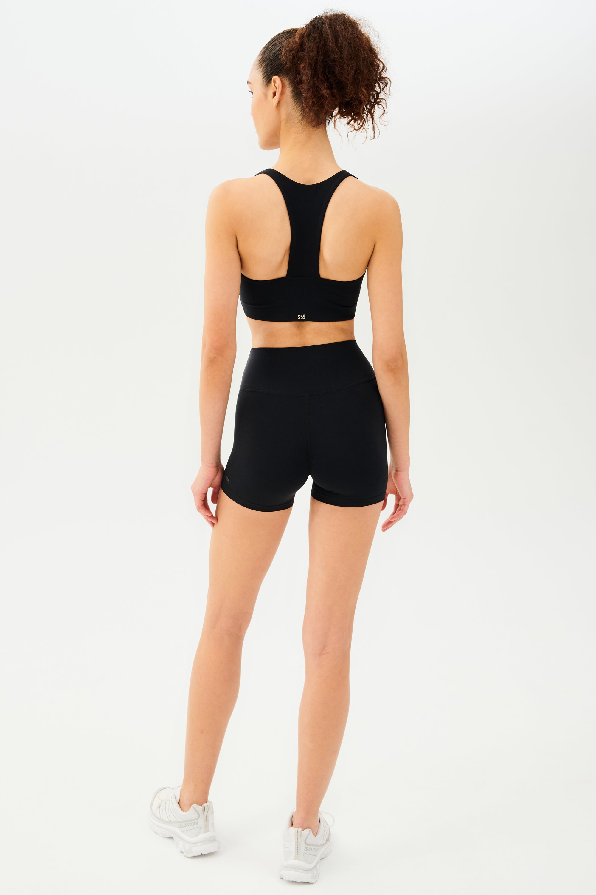 Full back view of girl wearing black shorts with black sports bra and white shoes