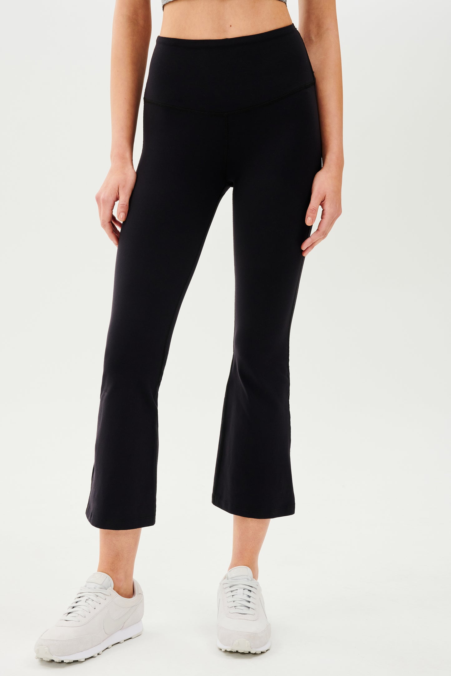A woman wearing SPLITS59's Raquel High Waist Crop leggings in black and a white tee.